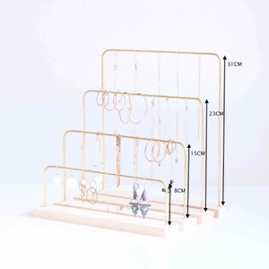 Pode incluir: Suporte de joias de metal dourado com tr&ecirc;s n&iacute;veis para colares e brincos. O suporte mede 31 cm de altura, 23 cm de largura e 8 cm de profundidade. Tem uma base de madeira.