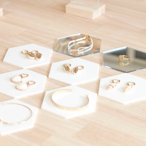Könnte beinhalten: Ein Schmuckset, das auf sechseckigen weißen Tabletts ausgestellt ist. Der Schmuck umfasst Ohrringe, ein Armband, einen Ring und eine Halskette. Der Schmuck ist aus Gold und hat ein Muschelthema.