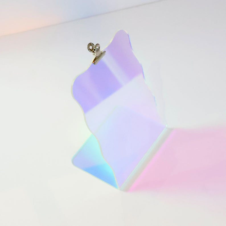 May include: A iridescent, holographic clipboard with a silver clip. The clipboard is standing upright on a white surface.