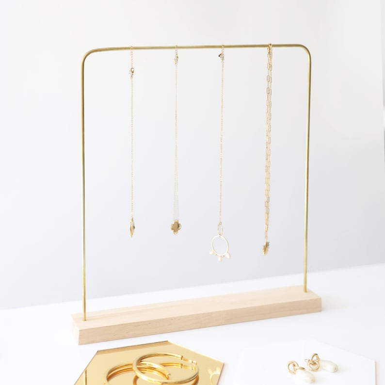 Pode incluir: Um suporte de joias de metal dourado com uma base de madeira. Cinco colares de ouro com diferentes pingentes est&atilde;o pendurados no suporte.