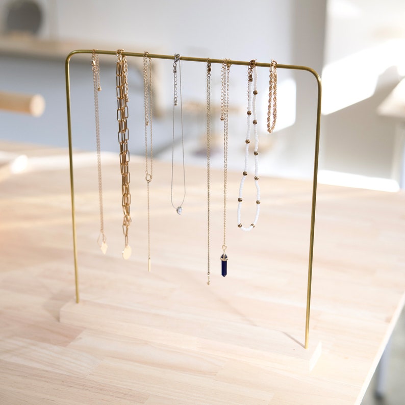Pode incluir: Um suporte de joias de metal dourado com sete colares pendurados nele. Os colares s&atilde;o feitos de diferentes materiais, incluindo correntes de ouro, contas e cristais.