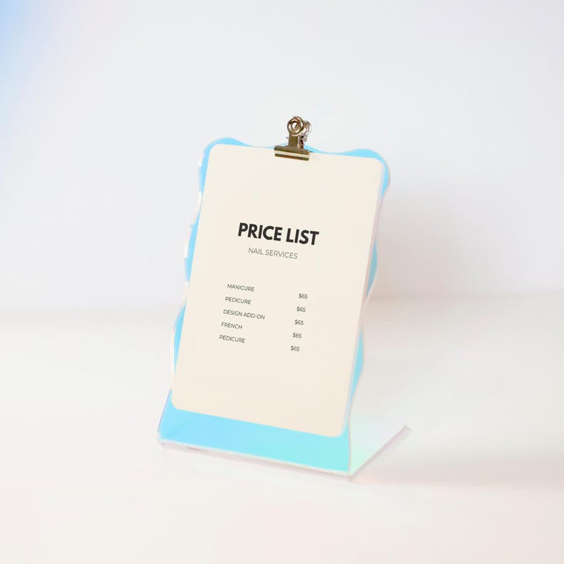 May include: A white price list sign with a blue iridescent frame and a silver clip. The sign lists prices for manicure, pedicure, design add-on, and french pedicure.