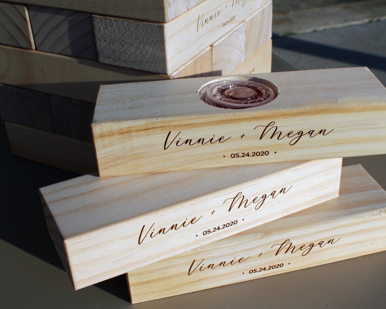 Puede incluir: Bloques de madera clara con la inscripci&oacute;n "Vinnie + Megan" y la fecha "05.24.2020". Un bloque tiene una hendidura circular. Los bloques parecen ser para un juego o decoraci&oacute;n.