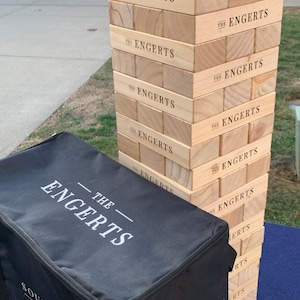 Puede incluir: Un juego de apilamiento de bloques de madera con el nombre "THE ENGERTS" impreso en cada bloque. Una bolsa de transporte negra con el mismo nombre est&aacute; en primer plano. El texto "UPGRADE TO A PERSONALIZED BAG! SEE DESCRIPTION FOR DETAILS." est&aacute; en la parte inferior.