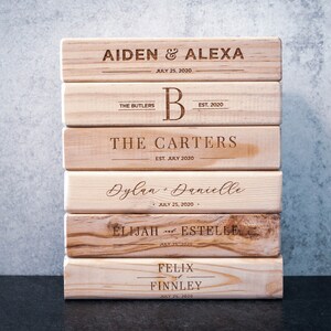 Puede incluir: Una pila de bloques de madera personalizados con nombres y fechas grabados. Los bloques presentan nombres como Aiden & Alexa, The Butlers, The Carters, Dylan & Danielle, Elijah & Estelle y Felix & Finnley, con fechas como el 25 de julio de 2020.