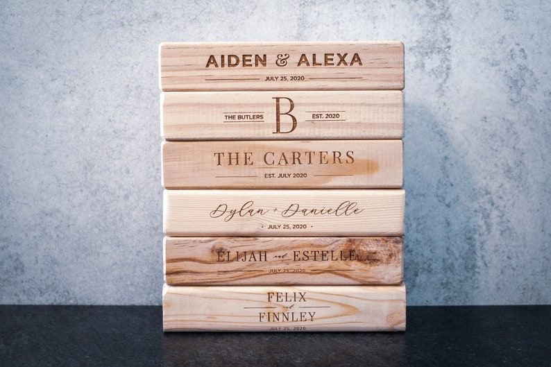 Puede incluir: Una pila de bloques de madera personalizados con nombres y fechas grabados. Los bloques presentan nombres como Aiden & Alexa, The Butlers, The Carters, Dylan & Danielle, Elijah & Estelle y Felix & Finnley, con fechas como el 25 de julio de 2020.