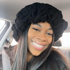 May include: A black, chunky-knit hat with a unique, textured design. The hat is made of a thick, dark yarn, creating a voluminous, stylish accessory. This handmade hat is perfect for adding a touch of flair to any outfit.