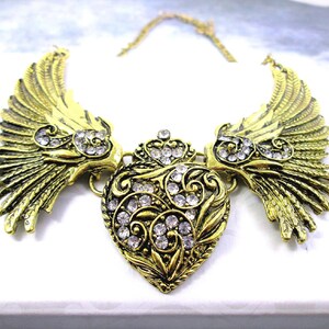 close-up shot of large angel wings with heart bib necklace in antique gold color