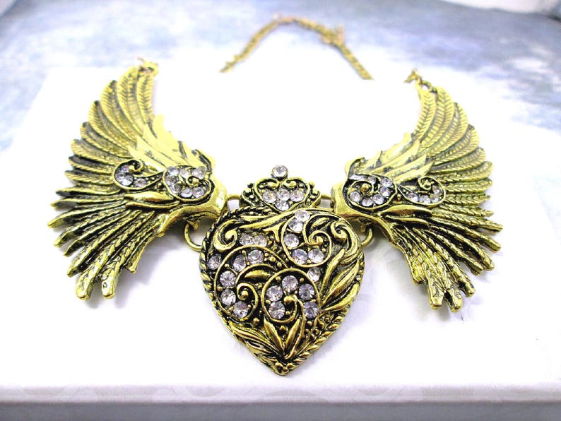 close-up shot of large angel wings with heart bib necklace in antique gold color