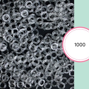 May include: A close-up image of a large quantity of clear plastic rings. The rings are scattered on a black surface. The number 1000 is written in white text on a pink circle with white polka dots.
