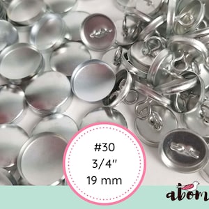 May include: A close-up of a pile of silver metal button blanks. The blanks are 3/4 inch (19 mm) in diameter and are labeled #30.