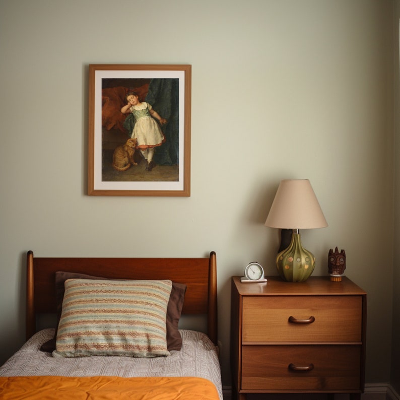 May include: A framed picture of a young girl in a green and white dress holding a small dog. The picture is hanging on a light green wall above a wooden dresser with two drawers.