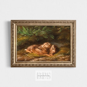 May include: A framed painting of two brown rabbits nestled together in a green mossy forest setting. The painting is in a gold frame with ornate details.