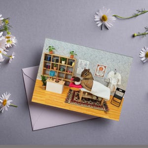 May include: A greeting card featuring a miniature spa scene with a chipmunk receiving a massage. The card shows a massage table, a small rug, a shelf with plants, and a white robe. Daisies and an envelope surround the card.