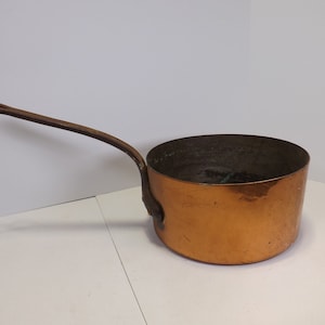 May include: A vintage copper saucepan with a wooden handle. The saucepan has a hammered finish and is in good condition.