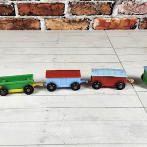 May include: A colorful toy train set with five cars. The train cars are painted in various colors, including green, yellow, red, and blue. The train is on a white wooden surface with a brick background. A classic toy for children.