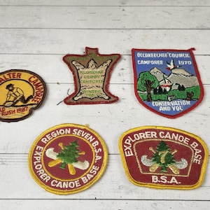 May include: A collection of vintage patches with various designs and text. One patch features a miner, another reads "Explorer Canoe Base B.S.A.", and another says "Belomeecher Council Camporee 1970". The patches are in shades of red, yellow, and blue.
