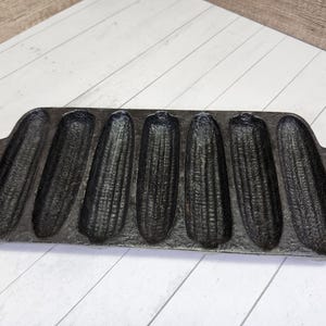 May include: A black cast iron cornbread pan with eight individual molds. The pan has two handles on the sides.
