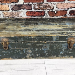 May include: A weathered wooden trunk with a distressed blue-green finish. The trunk features metal clasps and corner protectors, suggesting vintage or antique origins. The wood shows signs of wear, adding to its rustic charm.