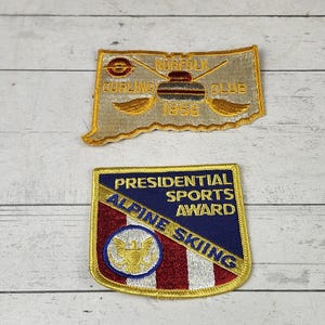 May include: Two embroidered patches. The top patch is gold with the words "Buffalo Curling Club 1958". The bottom patch is a shield shape with "Presidential Sports Award Alpine Skiing".