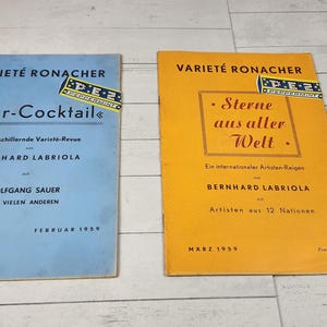 May include: Two vintage magazines titled "Varieté Ronacher" are displayed. One is light blue with "Star-Cocktail" on the cover, and the other is orange with "Sterne aus aller Welt." Both have text in German and are from 1959.