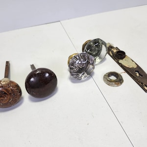 May include: Assortment of antique door knobs in various styles and materials, including glass, wood, and metal. The knobs are in various shades of brown, clear, and brass.