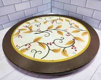 May include: Round decorative serving tray with a brown rim and a cream-colored center. The center features a design of gold-colored leaves, red berries, and green vines. The tray is approximately 16 inches in diameter.