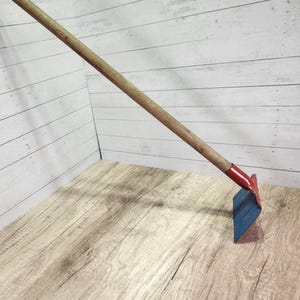 May include: A garden hoe with a wooden handle and a blue and red metal blade. The handle is long and angled, and the blade is rectangular. The tool is designed for gardening and landscaping.