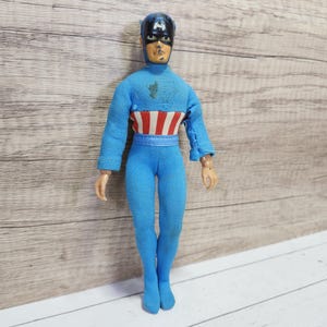 May include: A blue and red action figure of Captain America wearing a blue suit with a red, white, and blue star-spangled chest piece and a blue helmet with a white star.