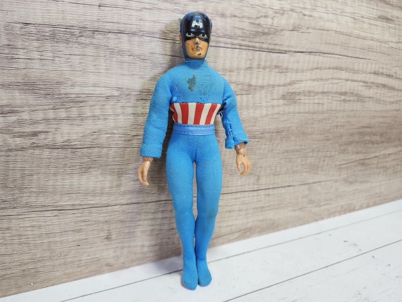 May include: A blue and red action figure of Captain America wearing a blue suit with a red, white, and blue star-spangled chest piece and a blue helmet with a white star.