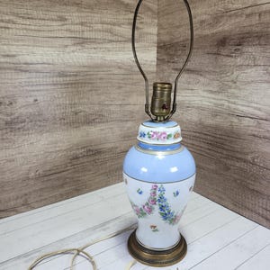 May include: A blue and white porcelain table lamp with floral designs. The lamp has a gold trim and a round base.