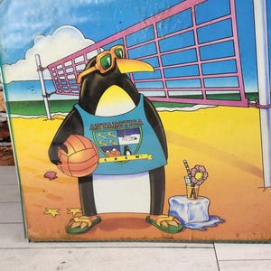 May include: A rectangular metal sign featuring a cartoon penguin wearing sunglasses and a blue tank top with the text Antarctica Crew. The penguin holds a volleyball on a sandy beach with a volleyball net, a drink, and a starfish in the background.