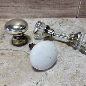 May include: Three vintage door knobs. One is silver, one is white porcelain, and one is clear glass.