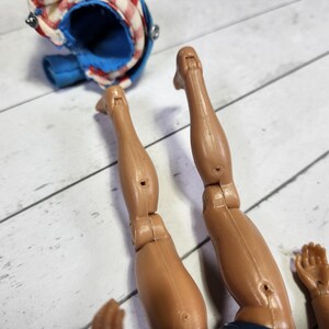 May include: Close-up of a pair of brown plastic legs with articulated knees. The legs are posed in a bent position, as if the figure is sitting or kneeling.