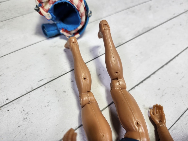 May include: Close-up of a pair of brown plastic legs with articulated knees. The legs are posed in a bent position, as if the figure is sitting or kneeling.
