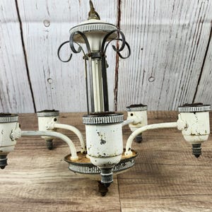May include: Vintage white and black chandelier with five arms. The chandelier has a distressed finish, with visible wear and tear. The arms extend outward, each holding a light socket. The fixture is designed for ceiling mounting.