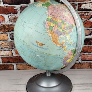 May include: A vintage globe with a light blue ocean and colorful continents. The globe is mounted on a silver-colored base and has a silver meridian ring. The background features a brick wall.