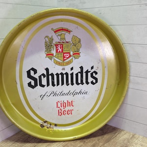 May include: Vintage Schmidt's Light Beer serving tray. The round metal tray has a gold rim and a white and gold center with the Schmidt's logo, a crest, and the words "Light Beer". The tray is slightly worn.