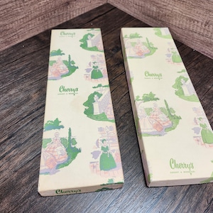 May include: Two rectangular boxes with a cream-colored background and a repeating pattern of figures in green, pink, and white. The boxes have the text "Cherry's" in a green script font.
