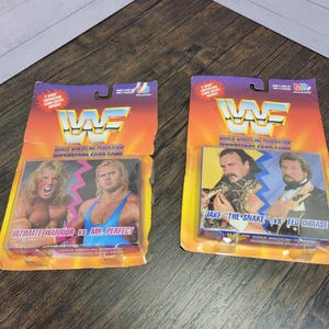 May include: Two WWF World Wrestling Federation Superstars Card Game packages. The left package features Ultimate Warrior vs. Mr. Perfect. The right package features Jake "The Snake" Roberts vs. Ted DiBiase.