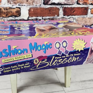 May include: A pink and purple Fashion Magic Jewelry Making Set box from the TV series Blossom. The box features the show's logo, images of jewelry, and the text "Create Funky Beads and Unique Jewelry To Wear!"