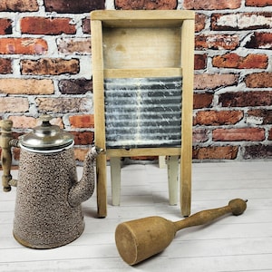 May include: An antique kitchen set featuring a speckled brown and white teapot, a wooden washboard, and a wooden mallet. The teapot has a silver lid and handle. The washboard has a metal scrubbing surface. The mallet is light brown.