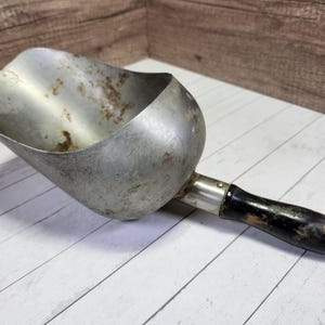 May include: A vintage metal scoop with a black wooden handle. The scoop is made of aluminum and has a worn, rustic look.