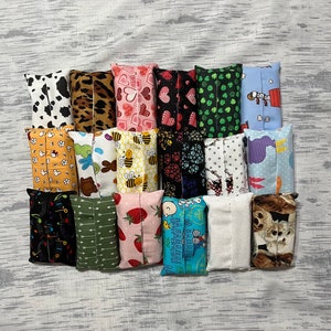 May include: A collection of rectangular fabric tissue box covers in various patterns. Designs include cow print, leopard print, hearts, shamrocks, bees, strawberries, arrows, and cartoon characters. The covers are in shades of white, black, pink, green, and blue.