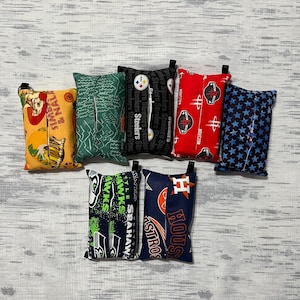 May include: A set of ten tissue box covers featuring various sports team logos. The covers are made of fabric and have a variety of colors and patterns. The logos include the Pittsburgh Steelers, Houston Astros, Seattle Seahawks, and more.