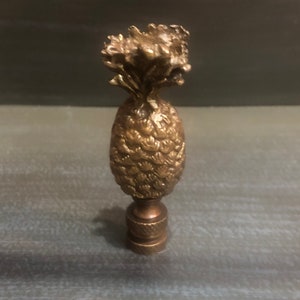 Puede incluir: Un embellecedor de lámpara de piña de color dorado con un diseño detallado.