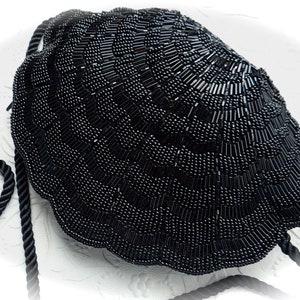 Puede incluir: Un bolso de noche negro de cuentas con forma de concha con un asa de cuerda negra.