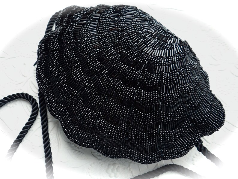 Puede incluir: Un bolso de noche negro de cuentas con forma de concha con un asa de cuerda negra.