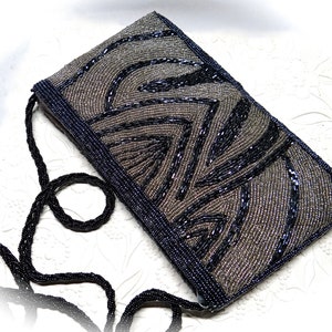 May include: A small, black and silver beaded evening bag with a long black beaded strap. The bag features a geometric pattern.