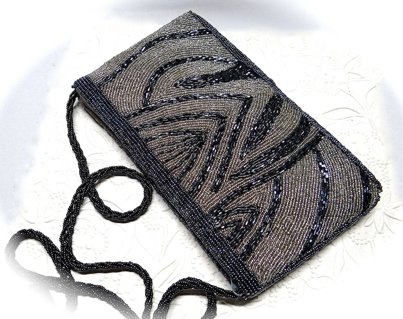 May include: A small, black and silver beaded evening bag with a long black beaded strap. The bag features a geometric pattern.